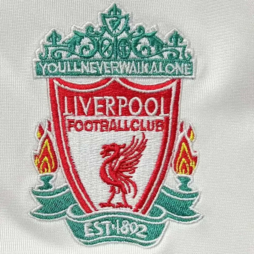Liverpool retro bortatröja 2006/08, närbild på broderat klubbmärke med leverfågel och texten You’ll Never Walk Alone